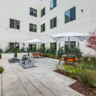 A modern outdoor courtyard featuring seating areas with umbrellas and lush greenery.