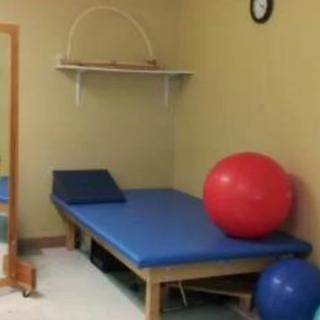 A physical therapy room featuring a blue treatment table and exercise balls.