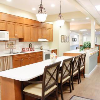 A modern kitchen interior featuring a long countertop with chairs, wooden cabinets, and elegant lighting.