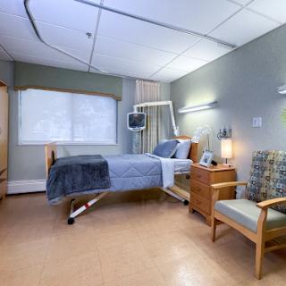 A clean and well-lit hospital patient room with a bed, seating area, and window.