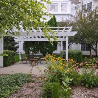 A serene garden with a white pergola and seating area surrounded by lush greenery and colorful flowers.