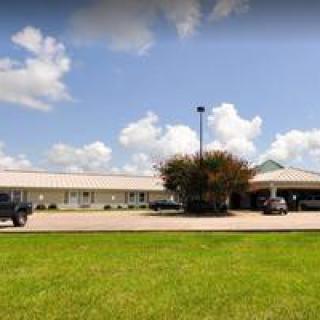 A single-story building with a parking lot and grassy area under a cloudy sky.