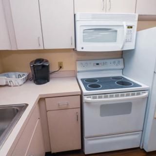 A compact kitchen corner featuring a stove with an overhead microwave and a coffee maker on the countertop.