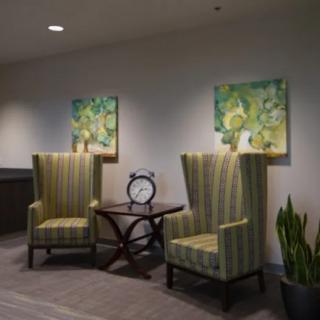 A cozy lounge area with two striped chairs, a small table with a clock, and vibrant paintings on the wall.