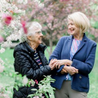 Two women enjoying a walk in a blossoming garden, sharing smiles and companionship.
