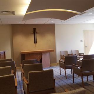 A serene chapel interior with rows of chairs facing an altar and a cross on the wall.