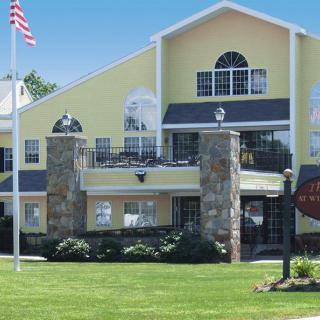 A sunny day view of a multistory residential building with a yellow exterior, stone details, and an American flag in front.