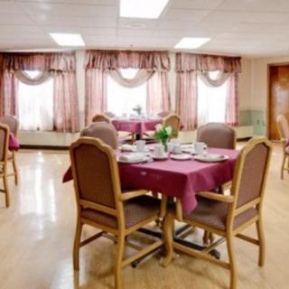 A dining area with multiple tables set for a meal, featuring elegant chairs and decorative curtains.