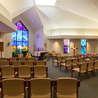 A chapel interior with rows of seating and vibrant stained glass windows.