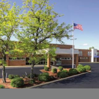 A building with an American flag, surrounded by trees and a parking lot.