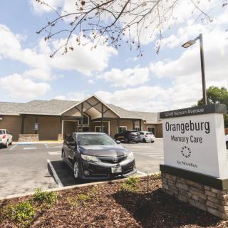 A nursing home with a parking lot and sign under a cloudy sky.