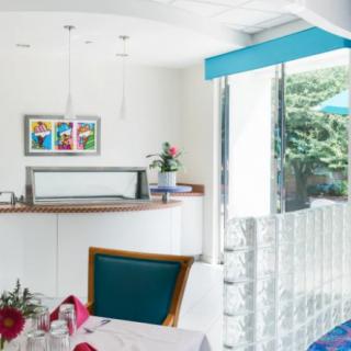 A modern and bright restaurant interior with colorful artwork, stylish furnishings, and a large window overlooking greenery.