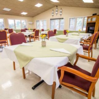 A well-lit dining room featuring multiple tables and chairs, each table covered with white and green tablecloths.