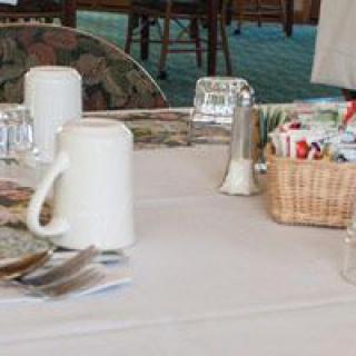 A dining table set with mugs, condiments, and a basket of items in a restaurant setting.