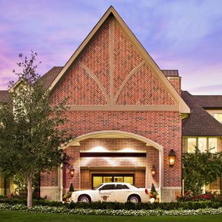 A grand brick building with a driveway and car parked under an entrance canopy during evening time.