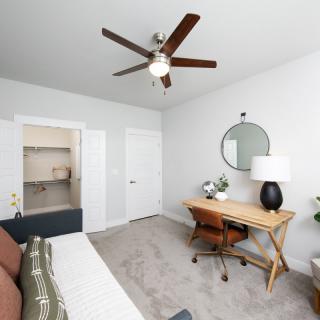 A modern bedroom with a desk, chair, and ceiling fan.