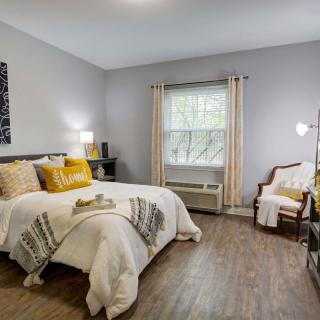 A cozy modern bedroom with natural lighting, featuring stylish decor and warm wooden flooring.