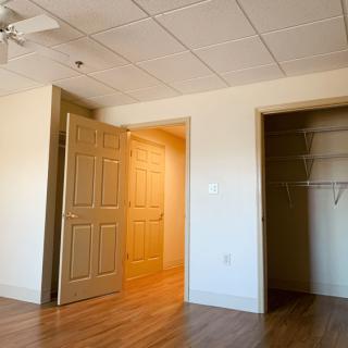 An empty room with hardwood flooring, featuring an open door, a closet, and a ceiling fan.