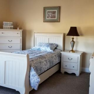 A cozy bedroom with a white bed, dresser, and nightstand.