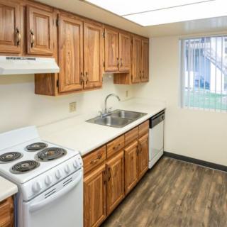 A compact kitchen with wooden cabinets, an electric stove, and laminate flooring.
