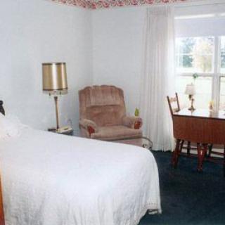 A cozy bedroom with a bed, armchair, desk, and lamp by the window.