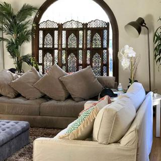 A cozy living room with plush sofas and decorative cushions, featuring a screen divider and an arched window.