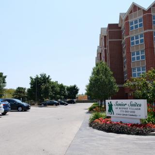 A view of an apartment complex with a parking lot and landscaped entrance.