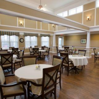 A spacious dining room with elegantly set tables and comfortable chairs, featuring large windows and warm lighting.