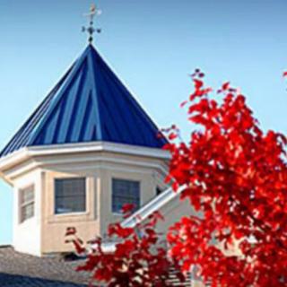 A building with a blue-roofed cupola and vibrant red autumn leaves in the foreground.
