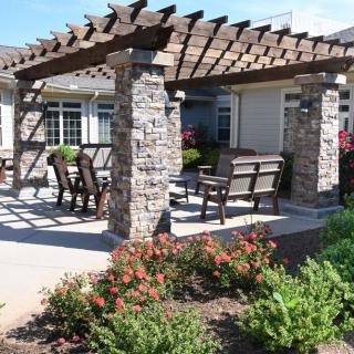 A beautiful outdoor pergola with stone columns, surrounded by a well-maintained garden and patio seating.