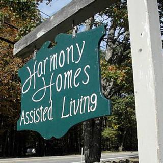 A wooden sign for Harmony Homes Assisted Living hanging outdoors.