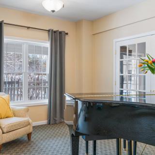 A cozy living room with a grand piano and a comfortable chair by the window.