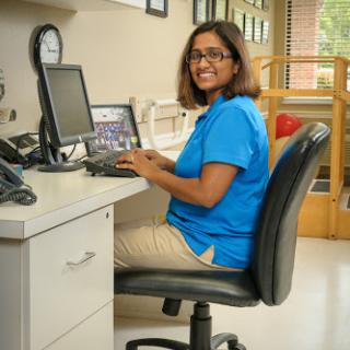 A person working on a computer in an office environment, smiling while seated at their desk.
