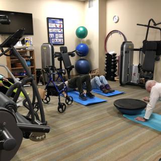 People exercising in a gym with various fitness equipment and yoga mats.