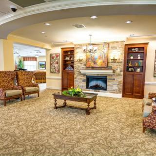 A cozy living room with a fireplace, armchairs, and a coffee table surrounded by bookshelves and decorative art.
