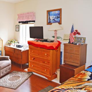 A cozy bedroom with wooden furniture, including a dresser and a TV, alongside decorative items and an American flag.
