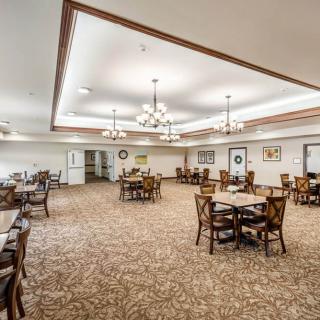 A spacious dining room with elegant chandeliers, arranged with multiple tables and chairs on a patterned carpet.