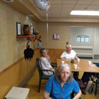 A group of seniors enjoying time together in an activity room, with decorations and a balloon adding to the festive atmosphere.