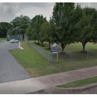 A small parking lot next to a fenced grassy area with trees.