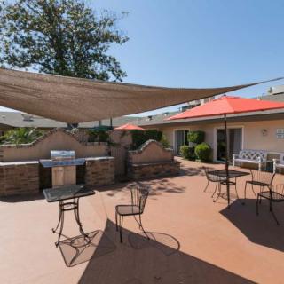 A sunny outdoor patio area with tables and chairs, shaded by a large sail canopy.