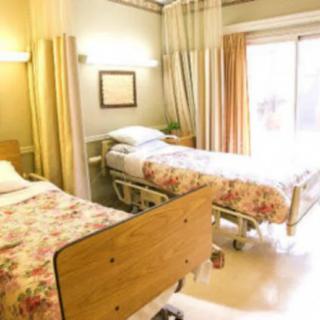 A hospital room with two neatly arranged beds and bright natural lighting.