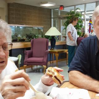 Two individuals enjoying a meal and engaging in conversation in a communal dining area.