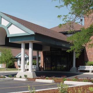 The image shows a building entrance with a canopy and an adjacent parking area.