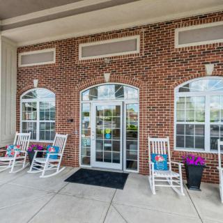 A building entrance with brick walls, large windows, and rocking chairs on the porch.