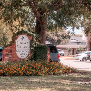 Entrance sign of an apartment complex surrounded by trees and parked cars.