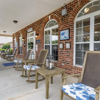 A welcoming porch with cushioned chairs set against a brick building with large windows.
