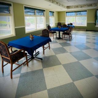 An empty dining room featuring blue tables and chairs, with large windows allowing natural light.
