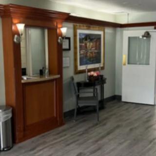 A small reception area featuring a wooden desk, a chair, a painting on the wall, and a door leading to another room.