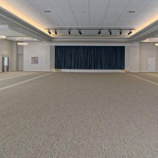 An empty conference hall with carpeted flooring and a stage with curtains.
