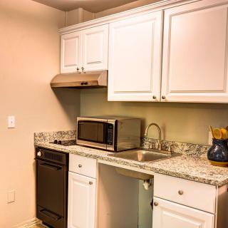 A modern kitchen with white cabinets and a granite countertop, featuring a microwave, sink, and dishwasher.